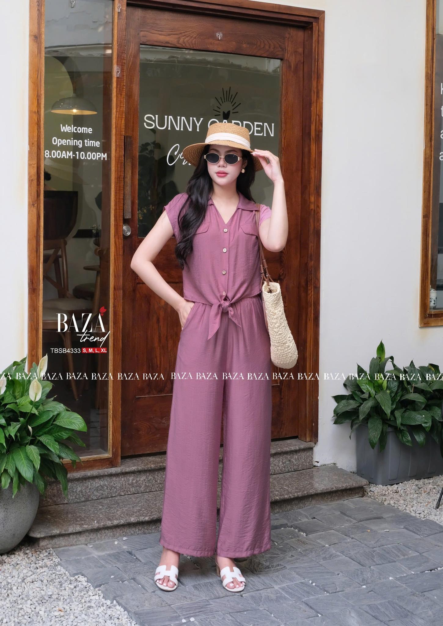 Bộ jumpsuit trung niên màu tím mận dáng dài, thiết kế không tay kèm hàng cúc trước và thắt eo nhẹ.